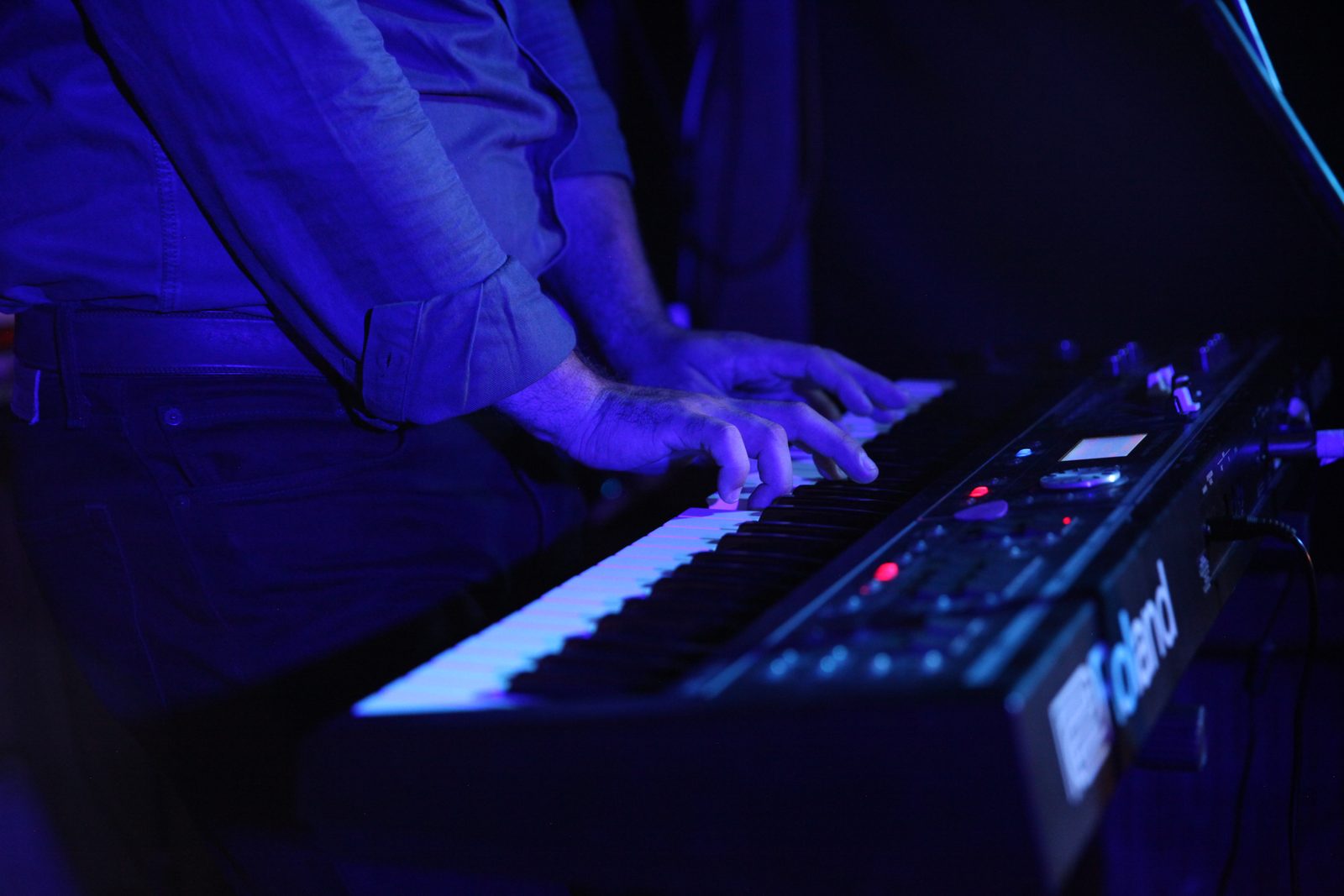 Hands playing a Roland keyboard under blue stage light